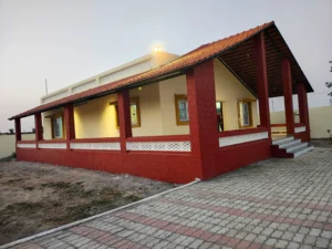 Farmhouse builder in Ranchi: finished farmhouse with terracotta-tiled veranda, red pillars and paver-block path