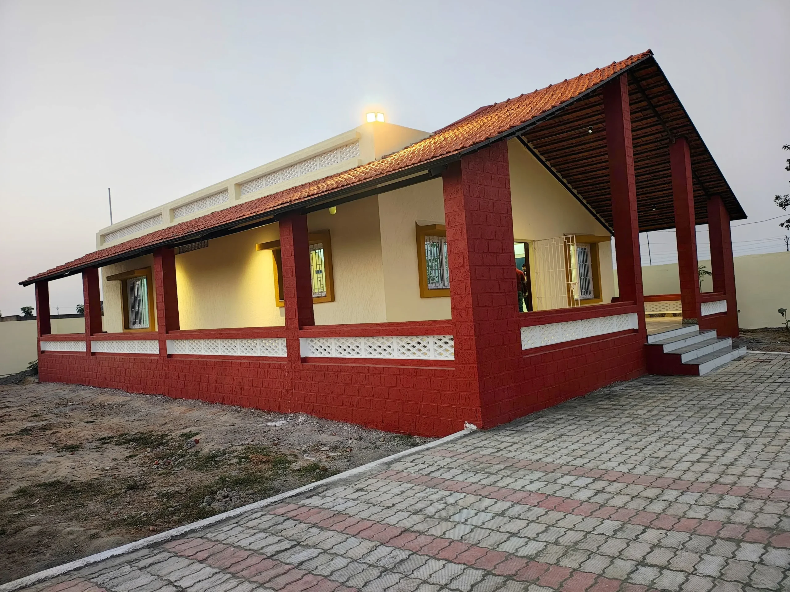 Farmhouse builder in Ranchi: finished farmhouse with terracotta-tiled veranda, red pillars and paver-block path