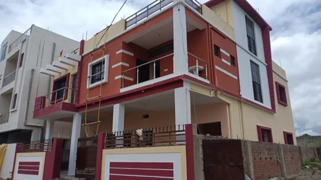 Corner view of a G+1 house in Argora Ranchi with covered parking, red-orange balcony and maroon-framed windows