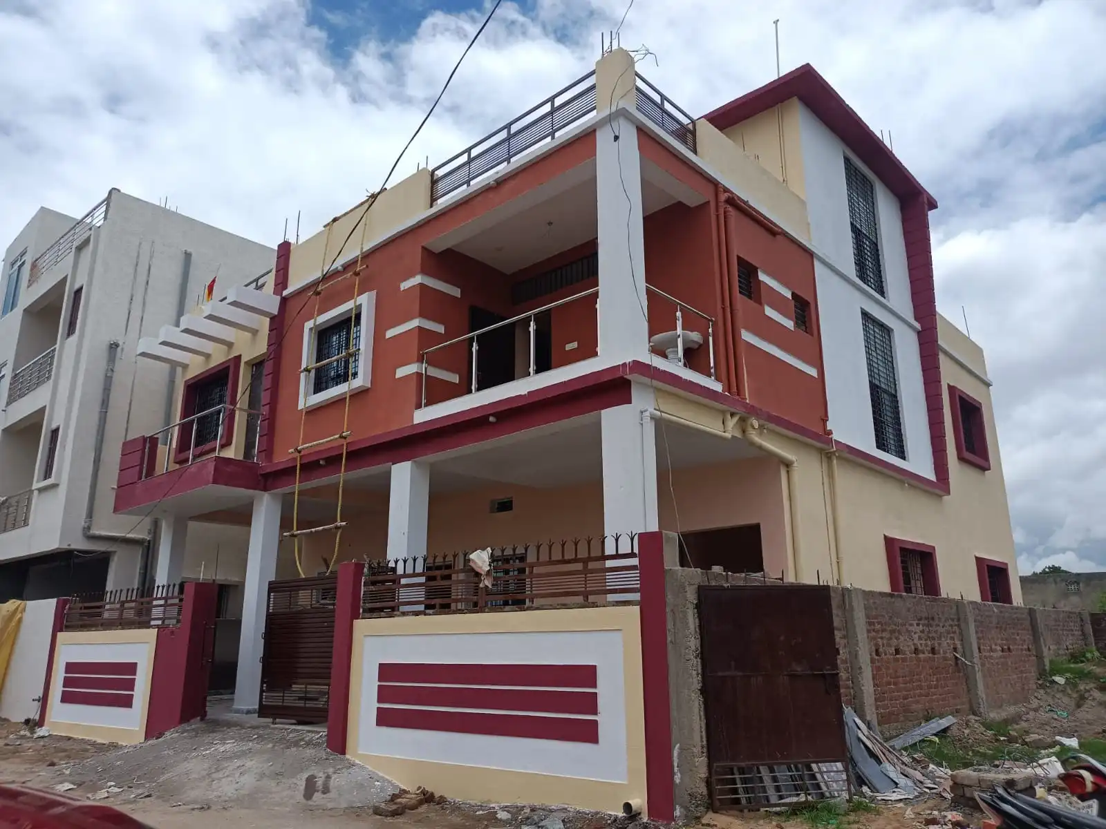 Corner view of a G+1 house in Argora Ranchi with covered parking, red-orange balcony and maroon-framed windows