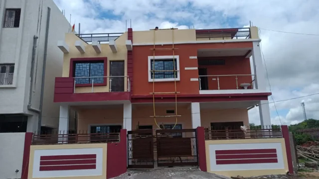 G+1 house construction in Ranchi: home with red-orange and yellow walls, maroon bands and brown slatted gate