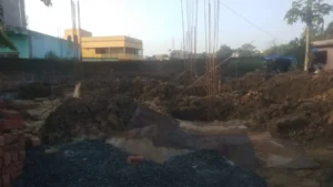 Foundation excavation with steel column bars and earth mounds at a house construction site in Ranchi