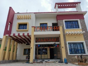 G+1 house design in Ranchi: finished maroon and beige family home with car porch, balcony and stone-look cladding