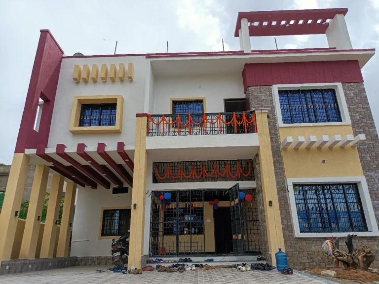 G+1 house design in Ranchi: finished maroon and beige family home with car porch, balcony and stone-look cladding