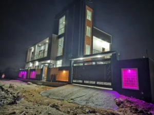 Night view of modern G+1 house in Ranchi with large gate, lit balcony and pink LED lights on compound wall