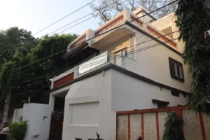 Old house renovation in Ranchi: renewed home with white textured walls, red jaali panel and glass balcony railing