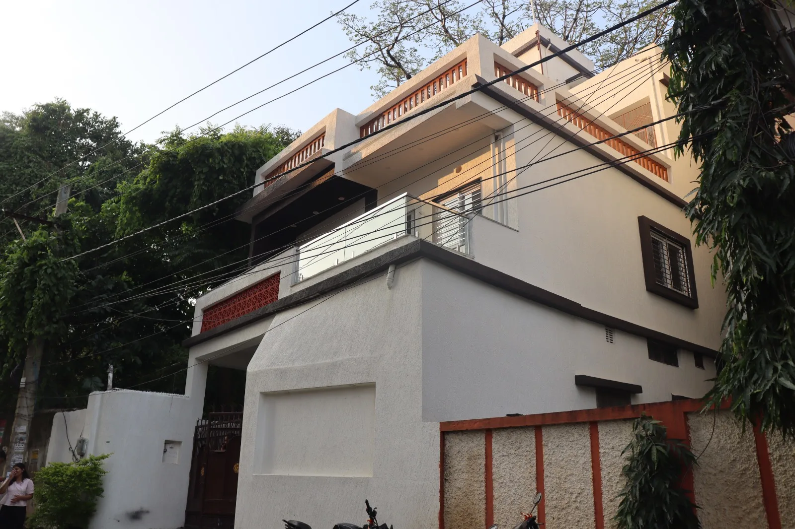 Old house renovation in Ranchi: renewed home with white textured walls, red jaali panel and glass balcony railing
